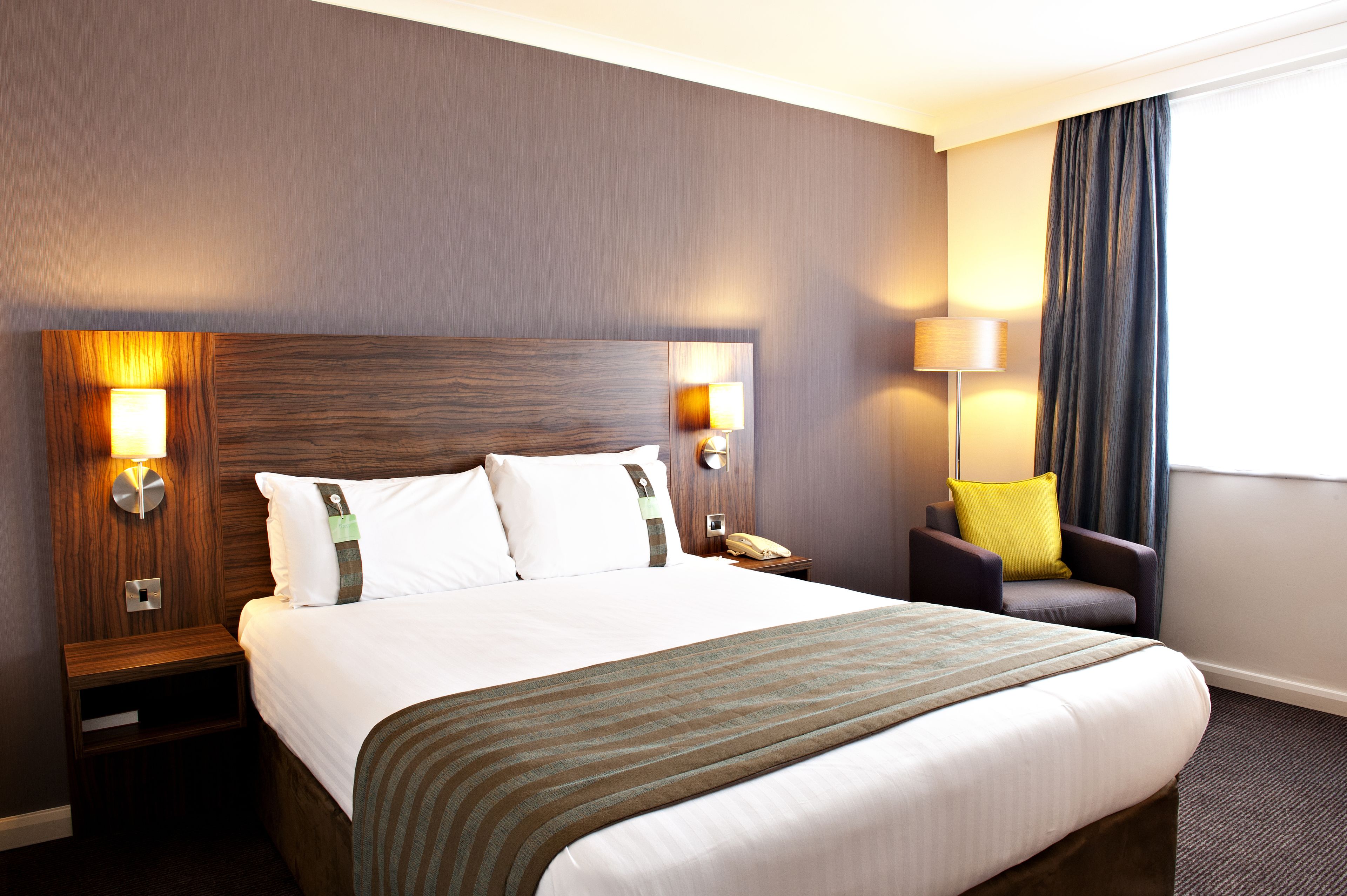 A hotel room with a large bed, two bedside tables, a chair, and a window with curtains.