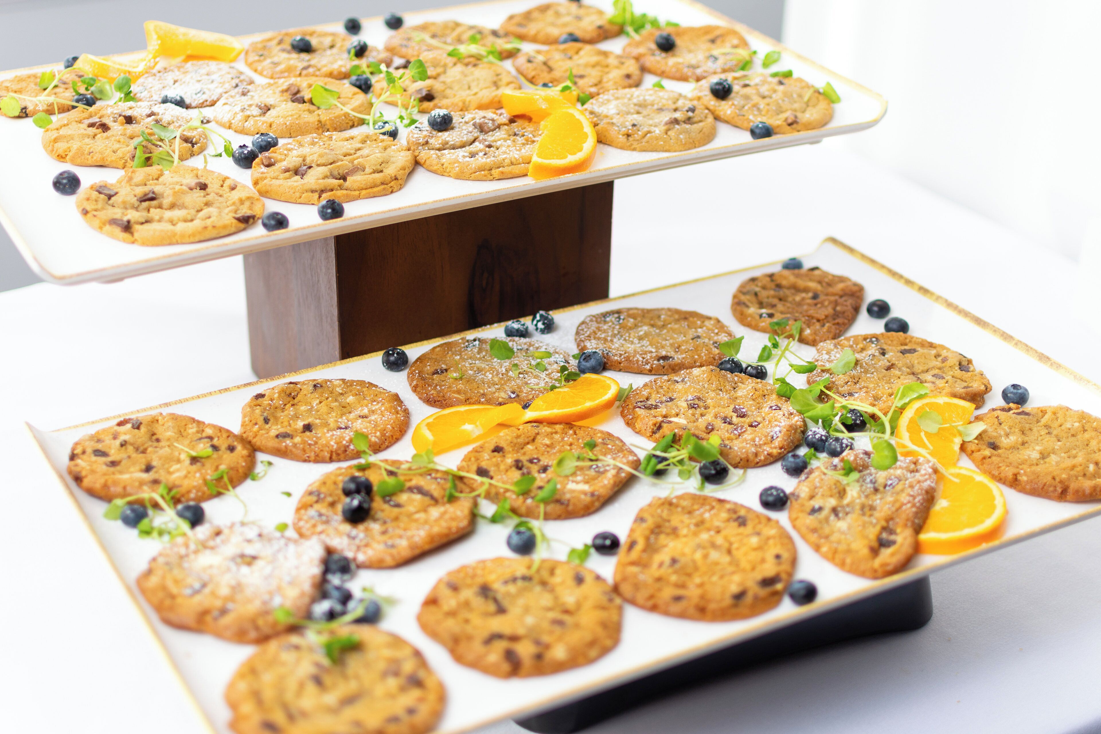 Two rectangular serving platters with cookies and garnishes.