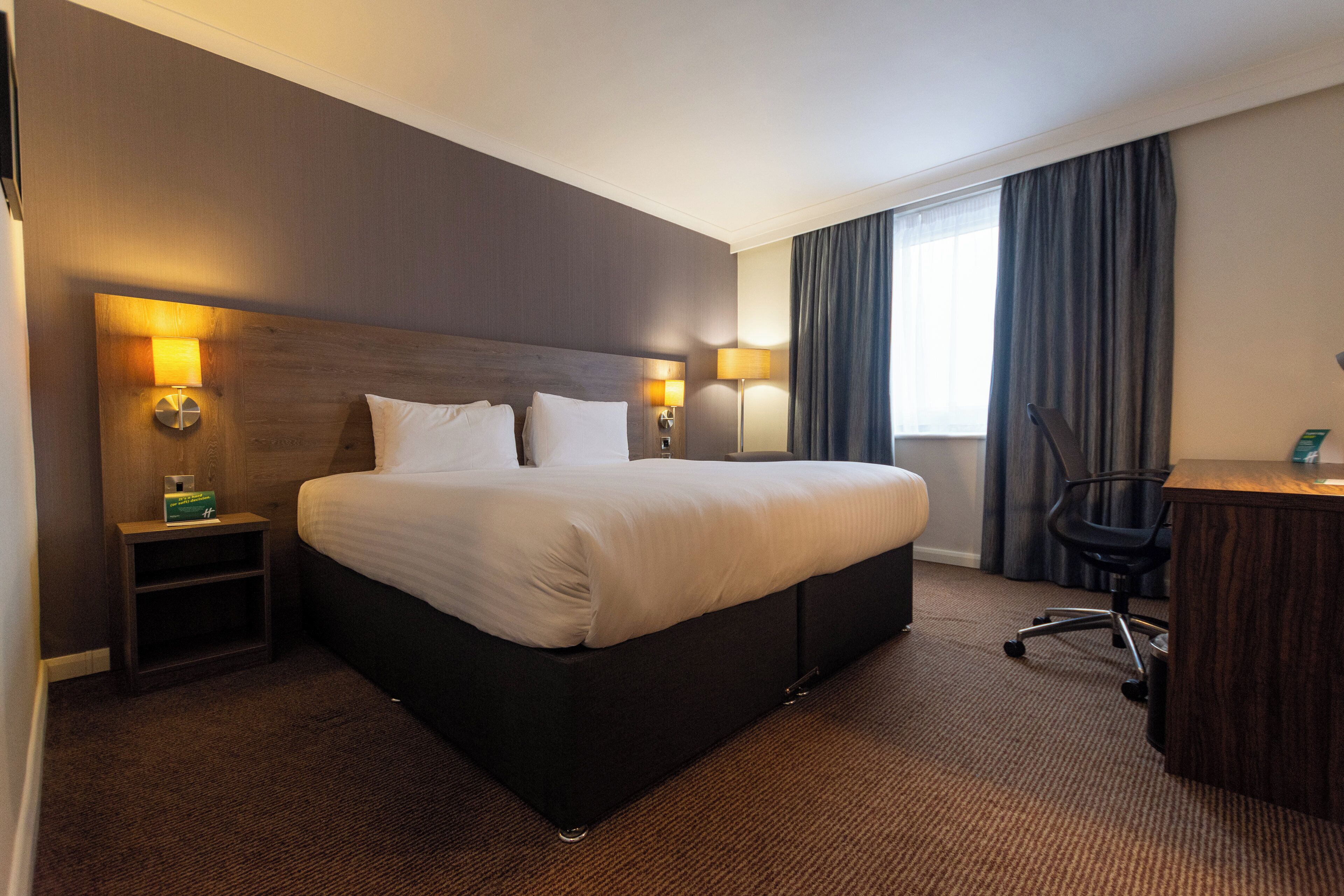 A hotel room with a large bed, two bedside lamps, a desk, and a chair.