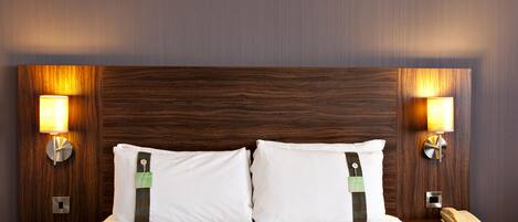 A hotel room with a large bed, two bedside tables, a telephone, and wall-mounted lamps.