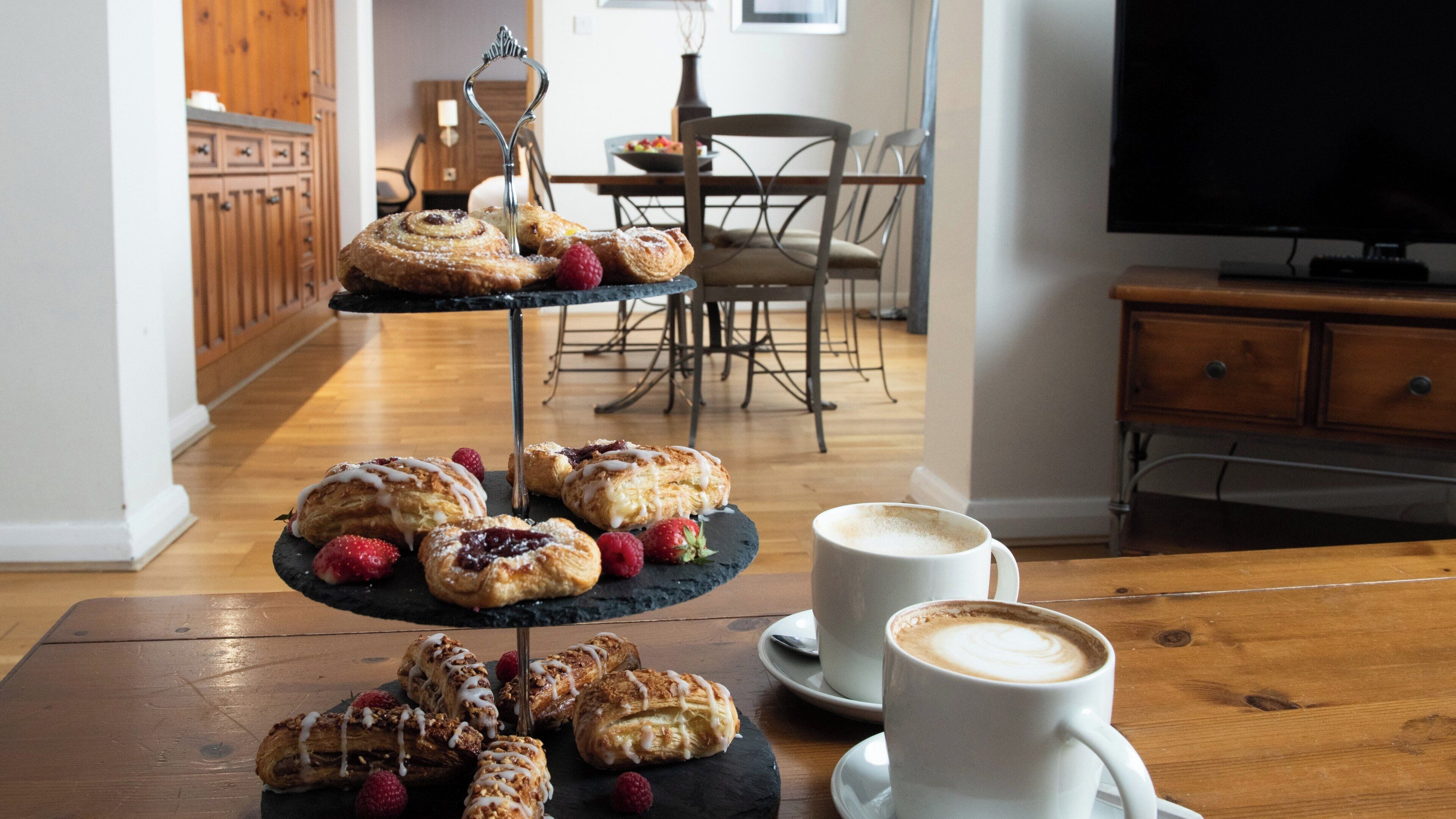 A three-tiered dessert stand with pastries and raspberries on a wooden table, accompanied by two white cups of coffee.