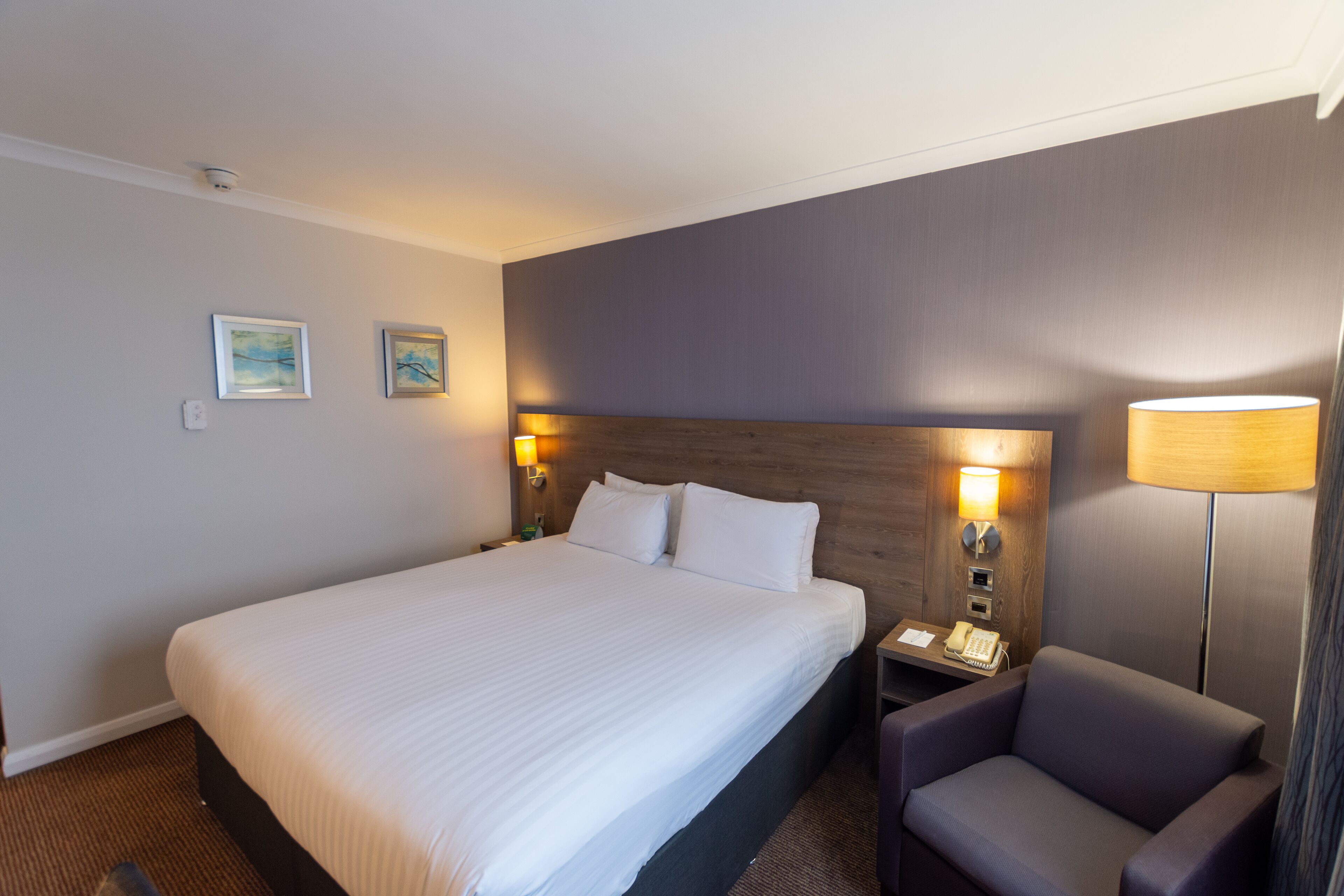 Habitación de hotel con una cama grande, dos lámparas de noche, una mesita con teléfono y una silla.