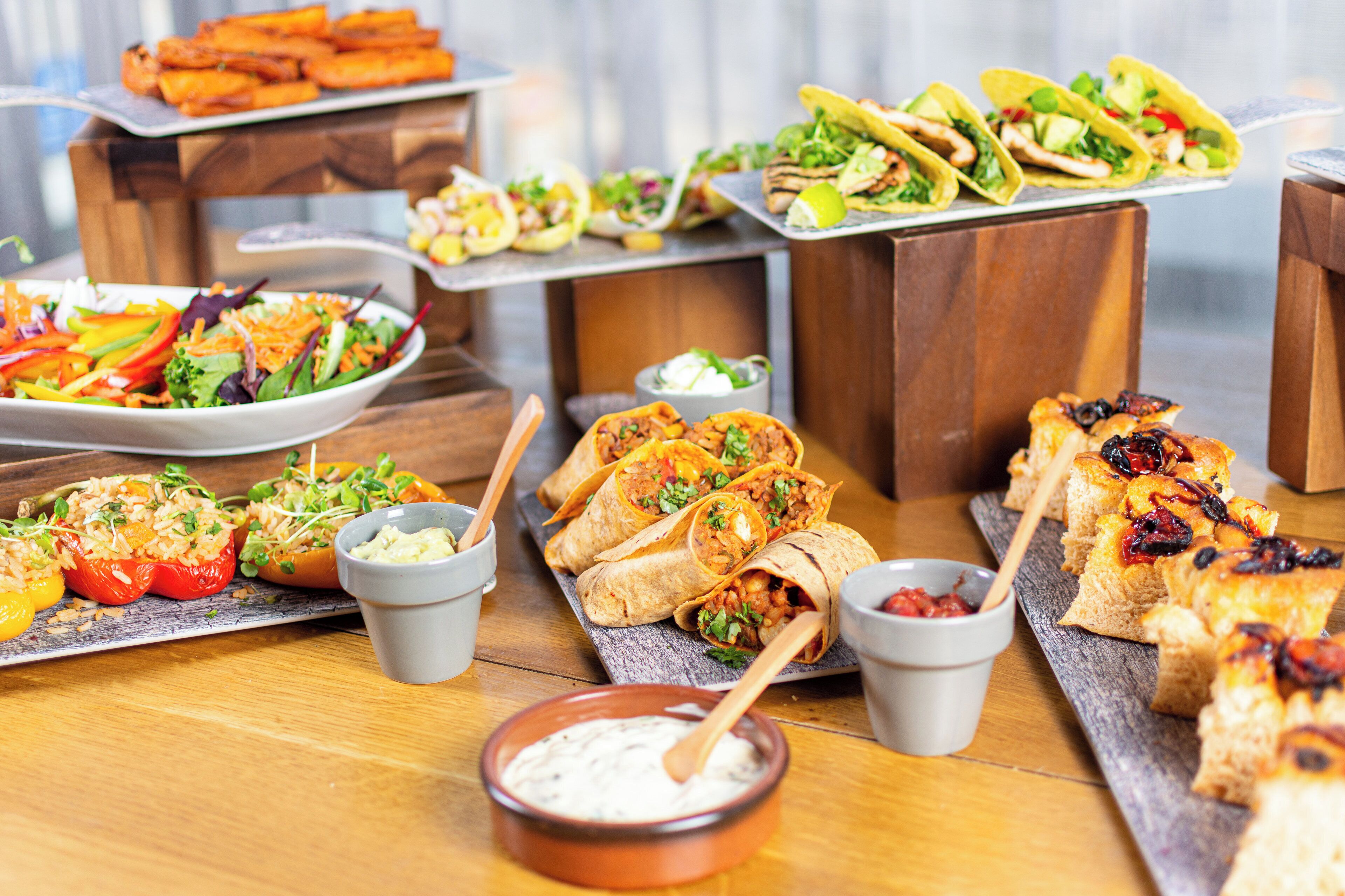 A variety of food items including tacos, burritos, and a salad, arranged on a wooden table.