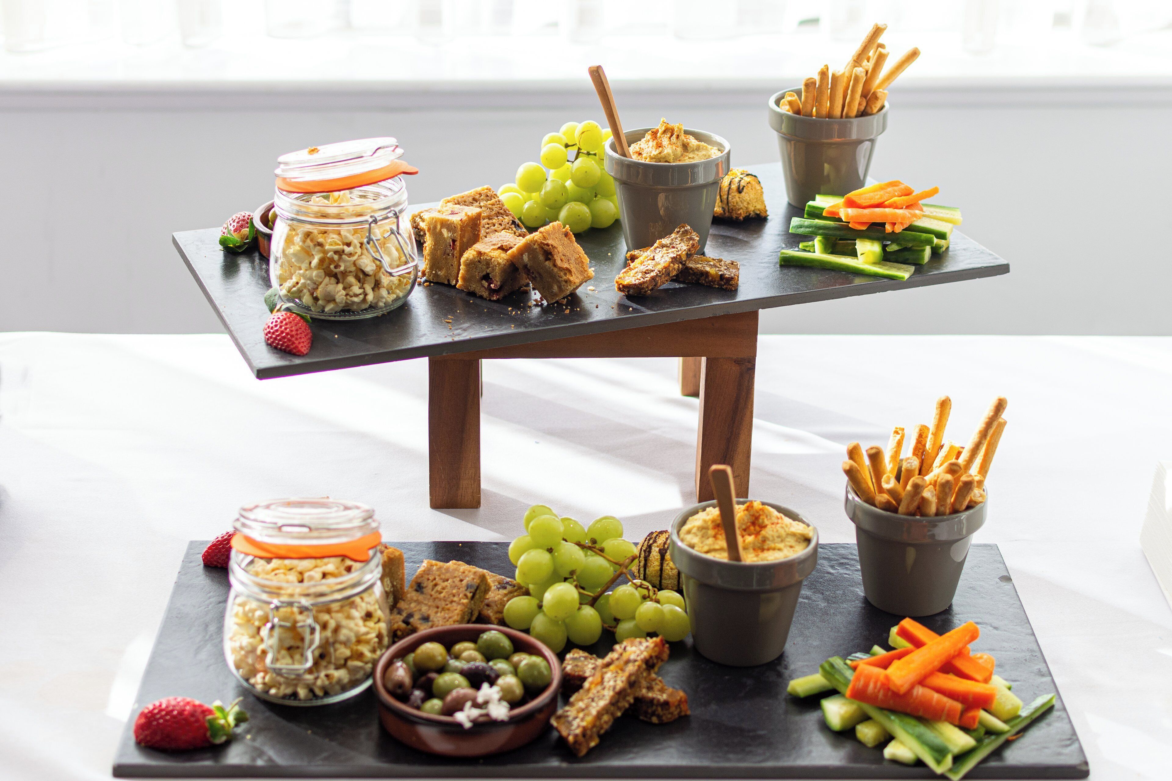 A two-tiered serving board with various snacks and fruits.