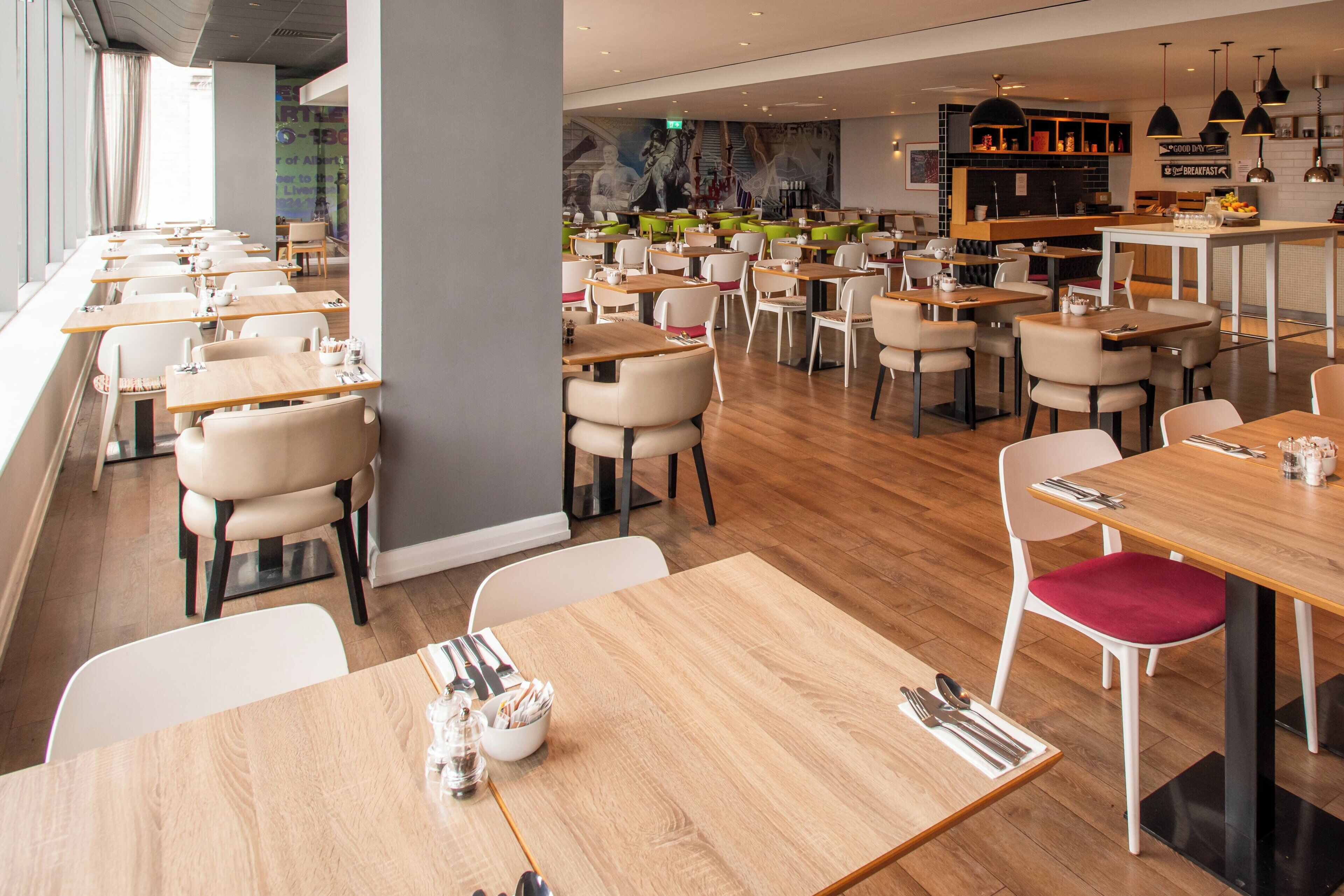 A modern restaurant with wooden tables and chairs, a bar area, and a mural on the wall.