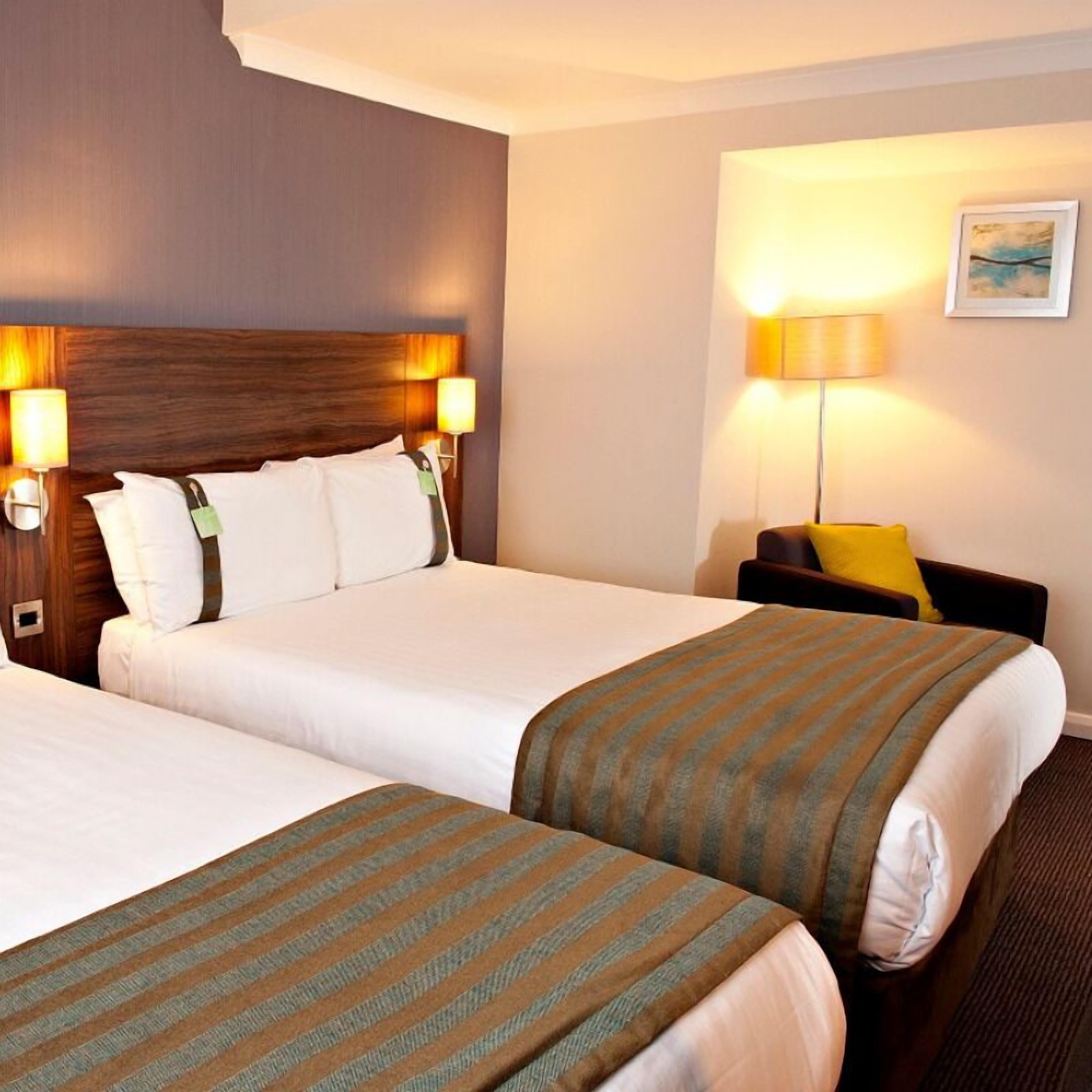 A hotel room with two beds, a wooden headboard, and two bedside lamps.