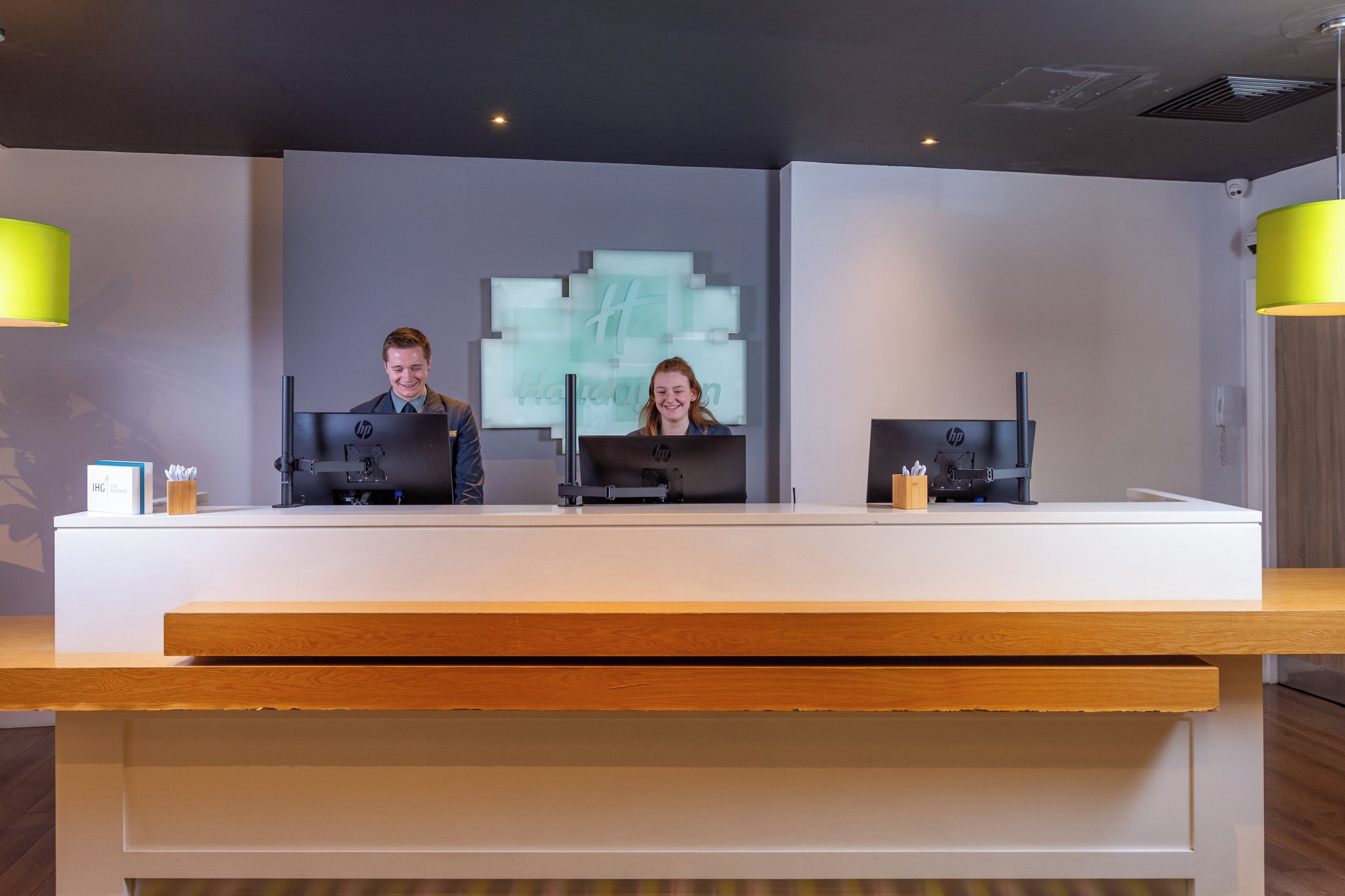 A reception desk with two HP computers, a 'Holiday Inn Express' sign, and a 'HP Rewards' sign.