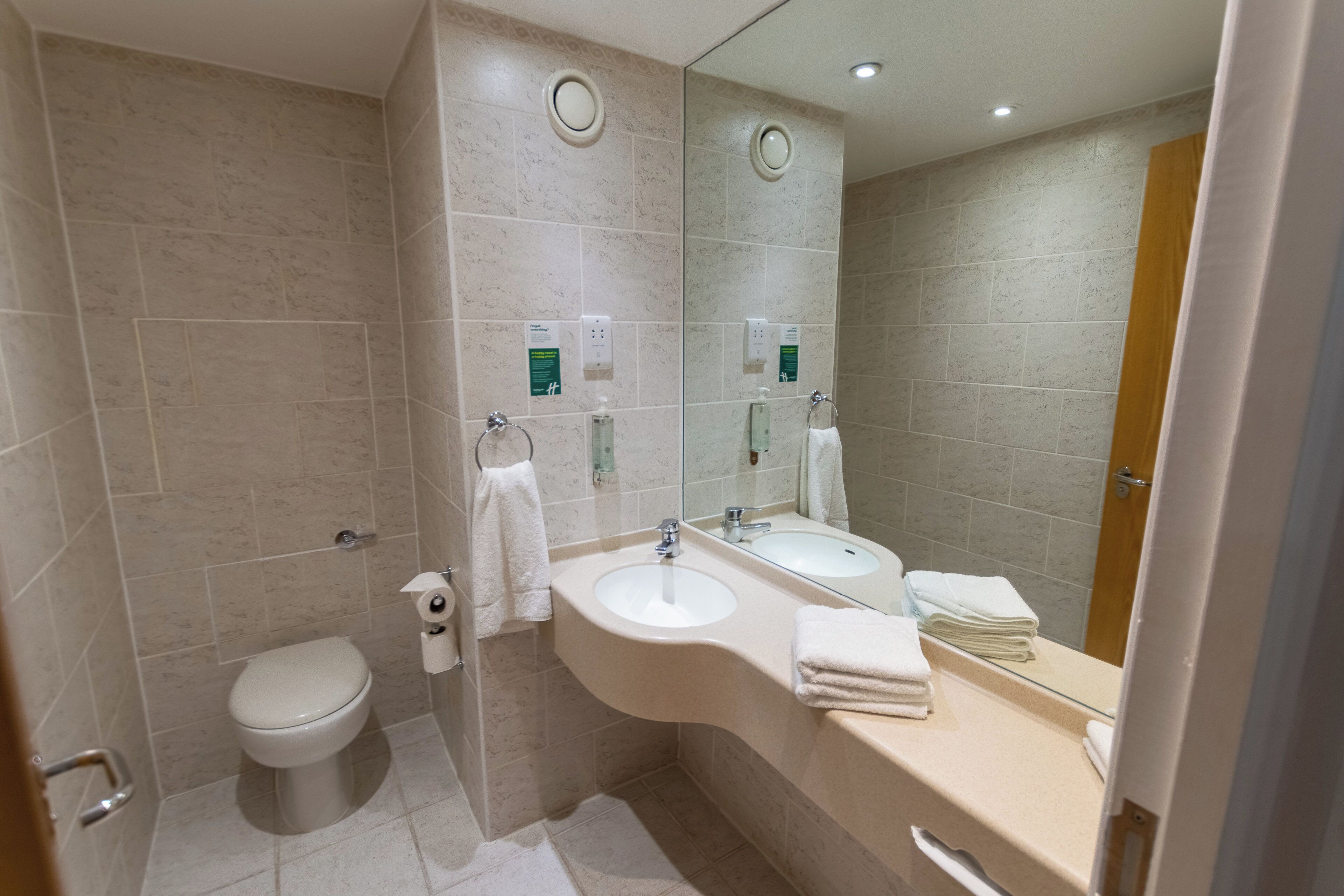 A modern bathroom with a toilet, two sinks, a mirror, and a towel rack.