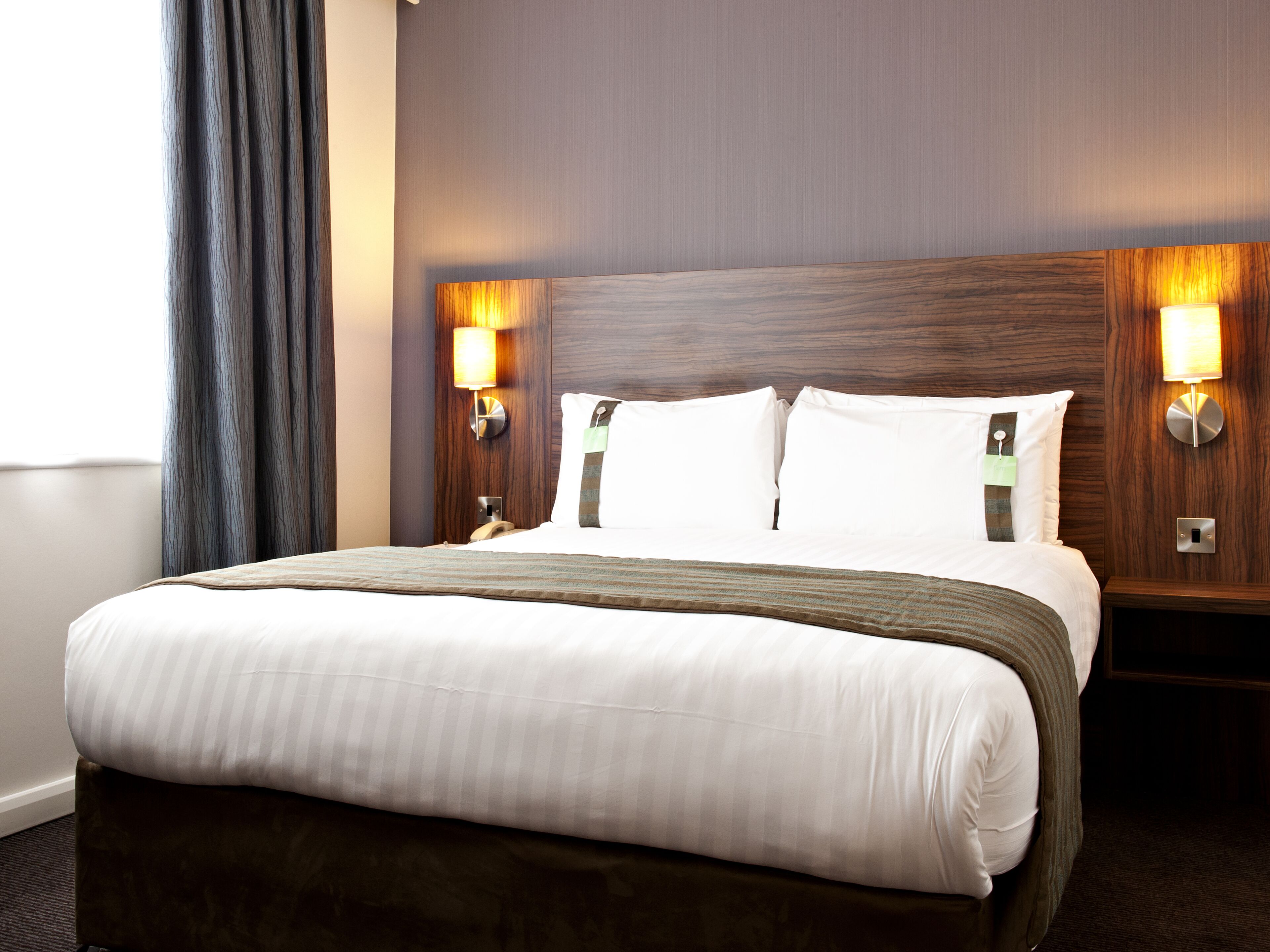 Une chambre d’hôtel avec un grand lit, deux lampes de chevet, une tête de lit en bois et une table de chevet avec un téléphone.