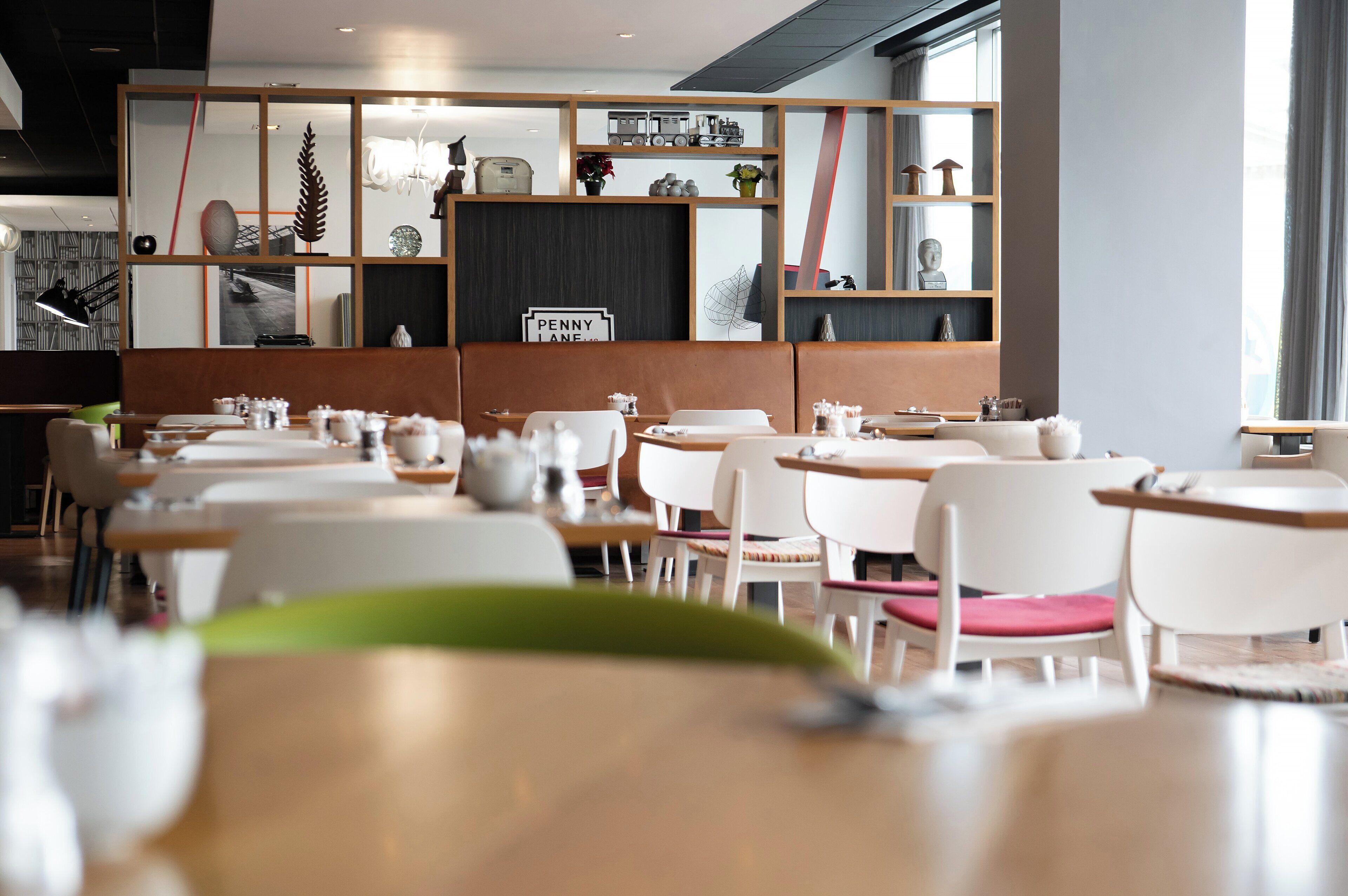L’intérieur d’un restaurant moderne, avec des chaises blanches, des tables en bois et divers objets décoratifs disposés sur des étagères.