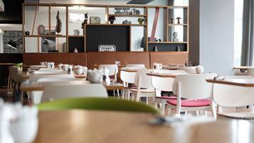 L’intérieur d’un restaurant moderne, avec des chaises blanches, des tables en bois et divers objets décoratifs disposés sur des étagères.
