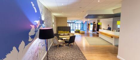 A modern hotel lobby with a large wall map, seating area, and a reception desk.