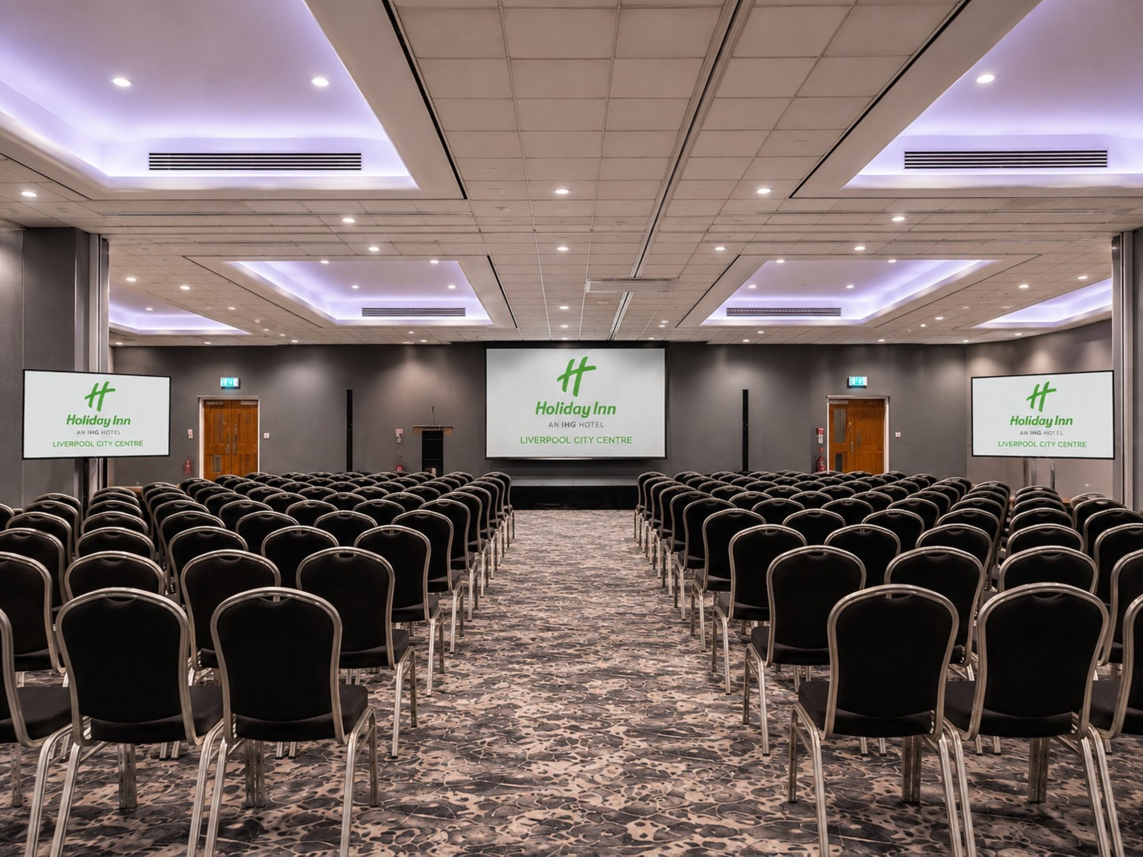 A conference room with rows of chairs facing a screen displaying the Holiday Inn logo.