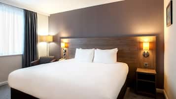 A hotel room with a large bed, two bedside lamps, a chair, and a window with curtains.