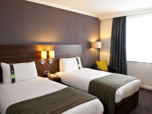 A hotel room with two beds, a nightstand with a telephone, a lamp, and a chair with a yellow pillow. - Holiday Inn Liverpool City Centre by IHG (Liverpool)