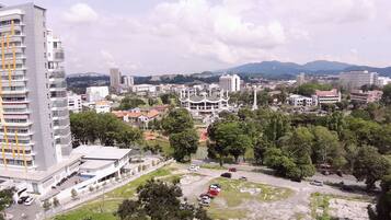 A high-rise building with a modern design, surrounded by a mix of residential and commercial buildings, and a park area with trees and a parking lot.