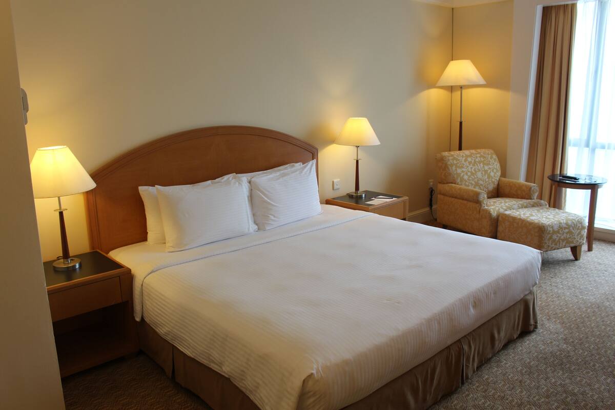 A hotel room with a large bed, two bedside lamps, a chair, and a small table.