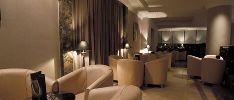 A modern hotel lobby with leather sofas, a coffee table, and a dining area in the background.