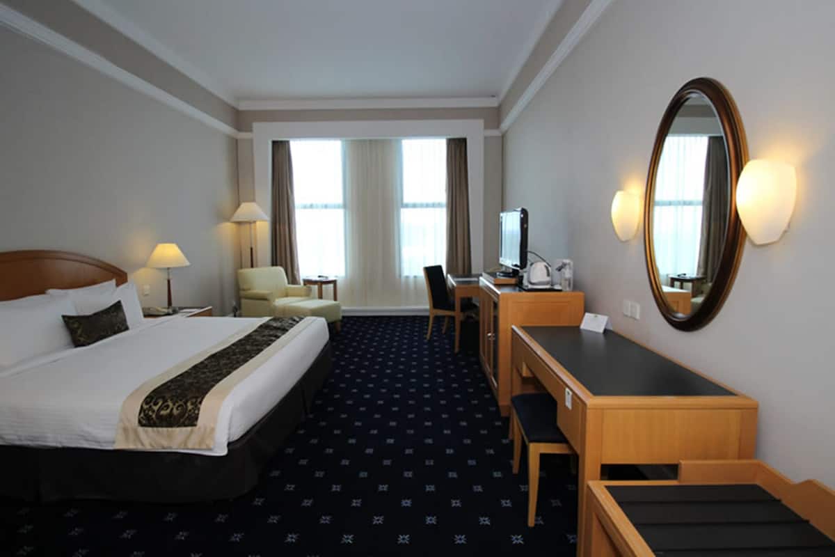 A hotel room with a large bed, a desk, a chair, a TV, and a mirror.