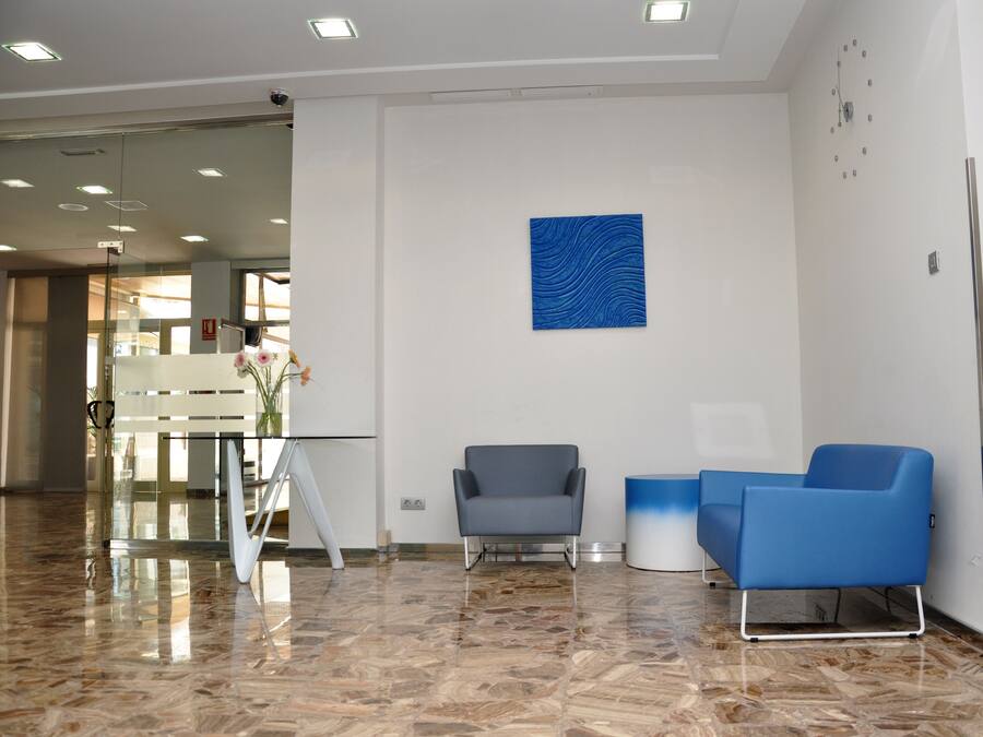 A modern lobby with a marble floor, two blue chairs, a grey chair, and a blue abstract painting on the wall.