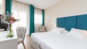 Una habitación de hotel con dos camas, un escritorio con un florero, una silla y un televisor.