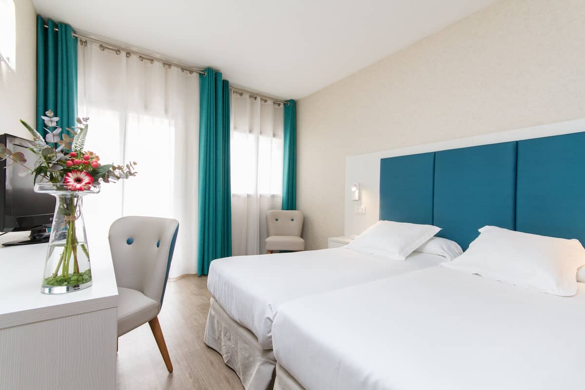 A hotel room with two beds, a desk with a vase of flowers, a chair, and a television.