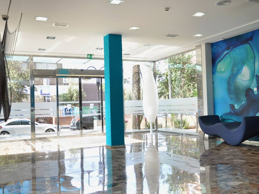 Un hall d’entrée moderne avec une entrée en verre, un pilier de couleur turquoise et une grande fresque murale abstraite.
