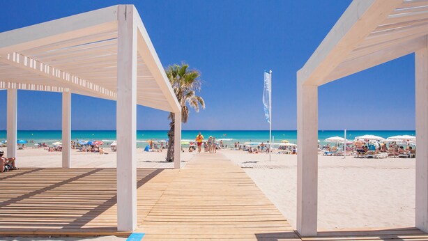 Una pasarela de madera que lleva a una playa con sombrillas y gente.