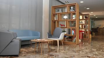A modern lobby with a blue sofa, a wooden bookshelf, and a marble floor.