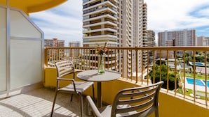 Un balcón con una mesa redonda y dos sillas, con vistas a una piscina y edificios altos.