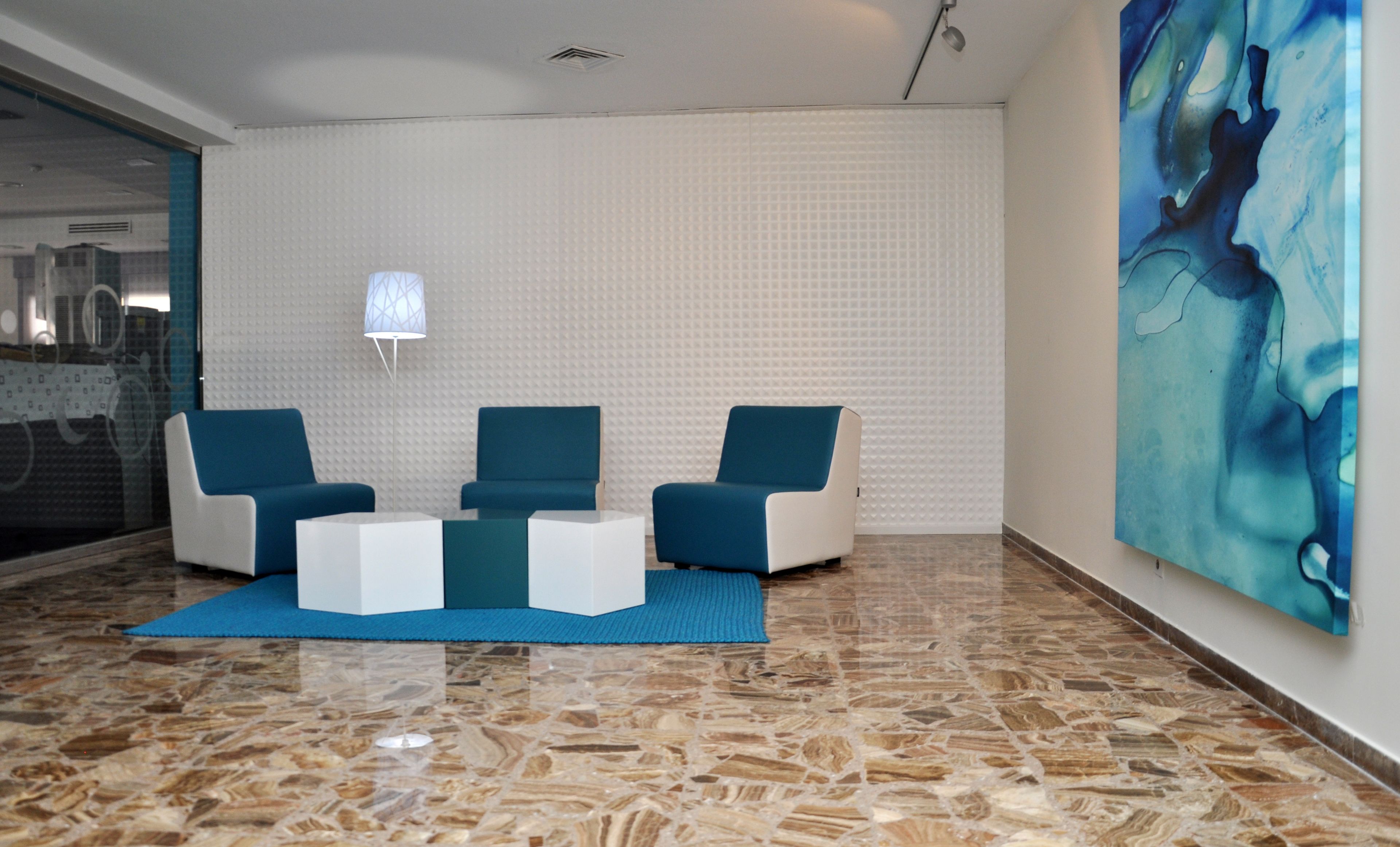A modern lobby with a marble floor, a blue sofa set, a white coffee table, and a large abstract painting on the wall.