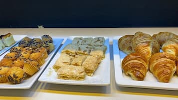 A buffet with various baked goods including muffins, a layered dessert, and croissants.