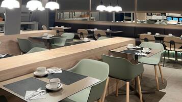 Een modern restaurant met lange gedeelde tafels en individuele zitjes, hangende verlichting en een grote spiegel die het interieur weerkaatst.