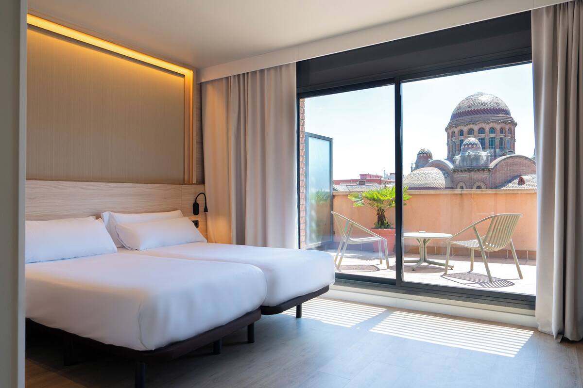 Habitación de hotel con una cama grande, vistas a un edificio con cúpulas y un balcón con sillas y una mesa.