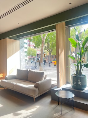 Une chambre d’hôtel moderne, équipée d’un canapé, d’une petite table, d’une plante en pot et d’une grande fenêtre donnant sur la rue.