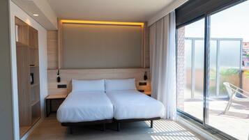 Habitación de hotel moderna con cama doble, estanterías empotradas, mesita de noche y un amplio ventanal con vistas al exterior.