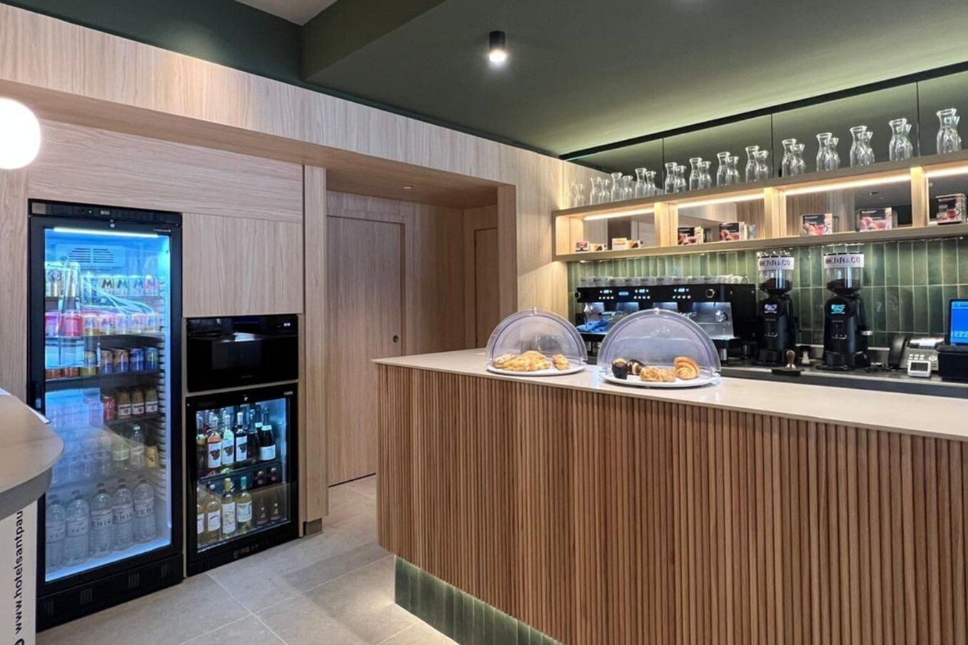 Una zona de bar moderna con mostrador de madera, vitrina refrigerada y estación de café.