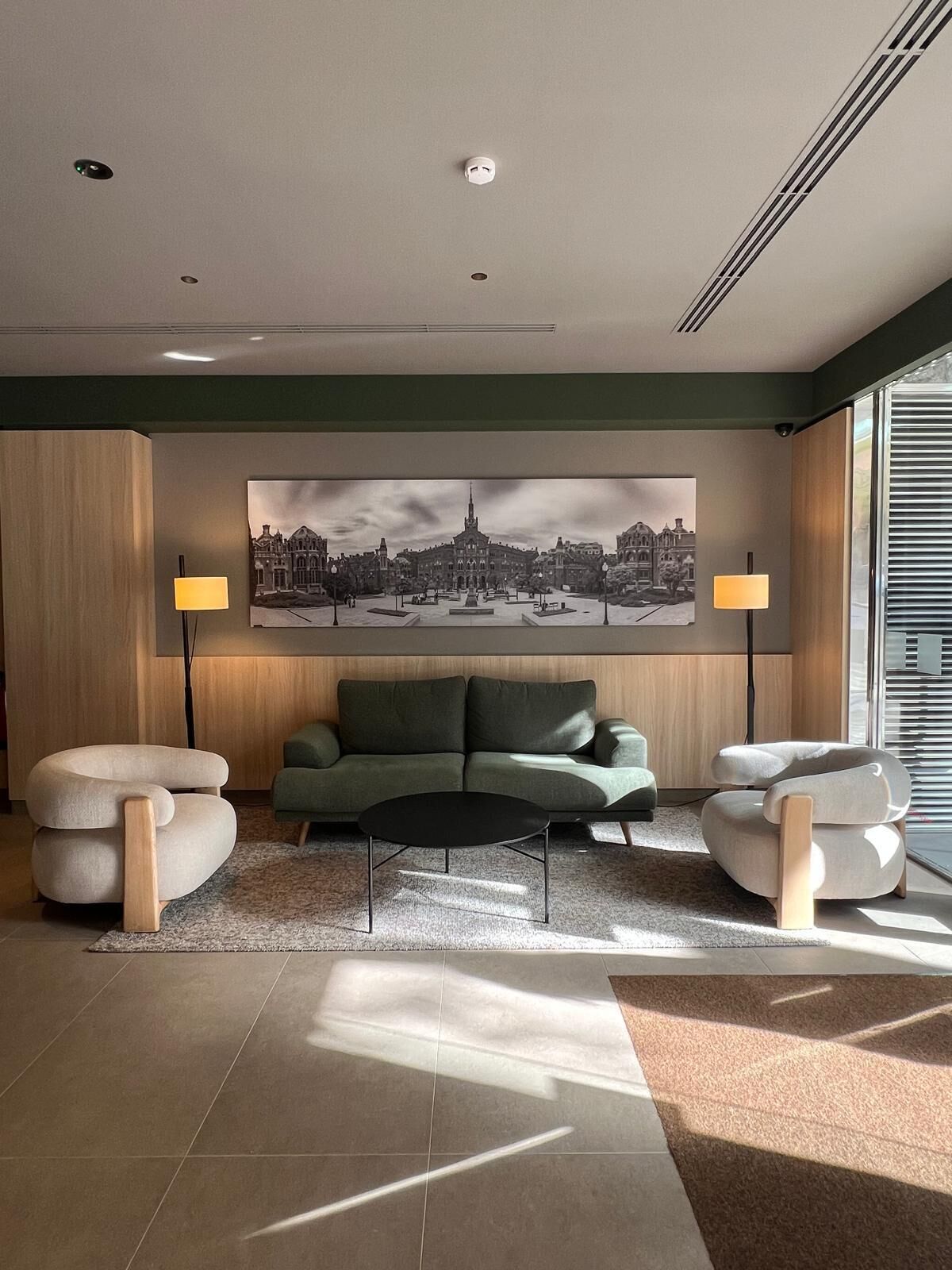 A modern living room with a green sofa, two armchairs, a black coffee table, and a large cityscape painting on the wall.