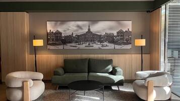 A modern living room with a green sofa, two armchairs, a black coffee table, and a large cityscape painting on the wall.