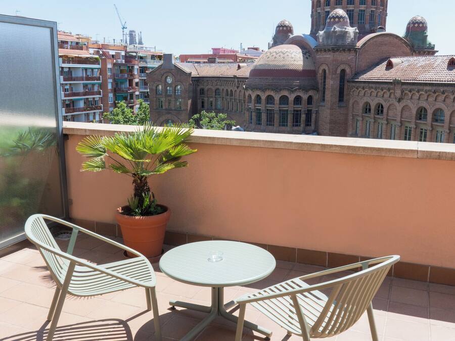 A balcony with two chairs and a table, overlooking a historic building with domed roofs.