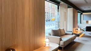 A modern hotel lobby with a wooden reception desk, seating area, and large windows offering a view of the street. - HOTEL SANT PAU (Barcelona)