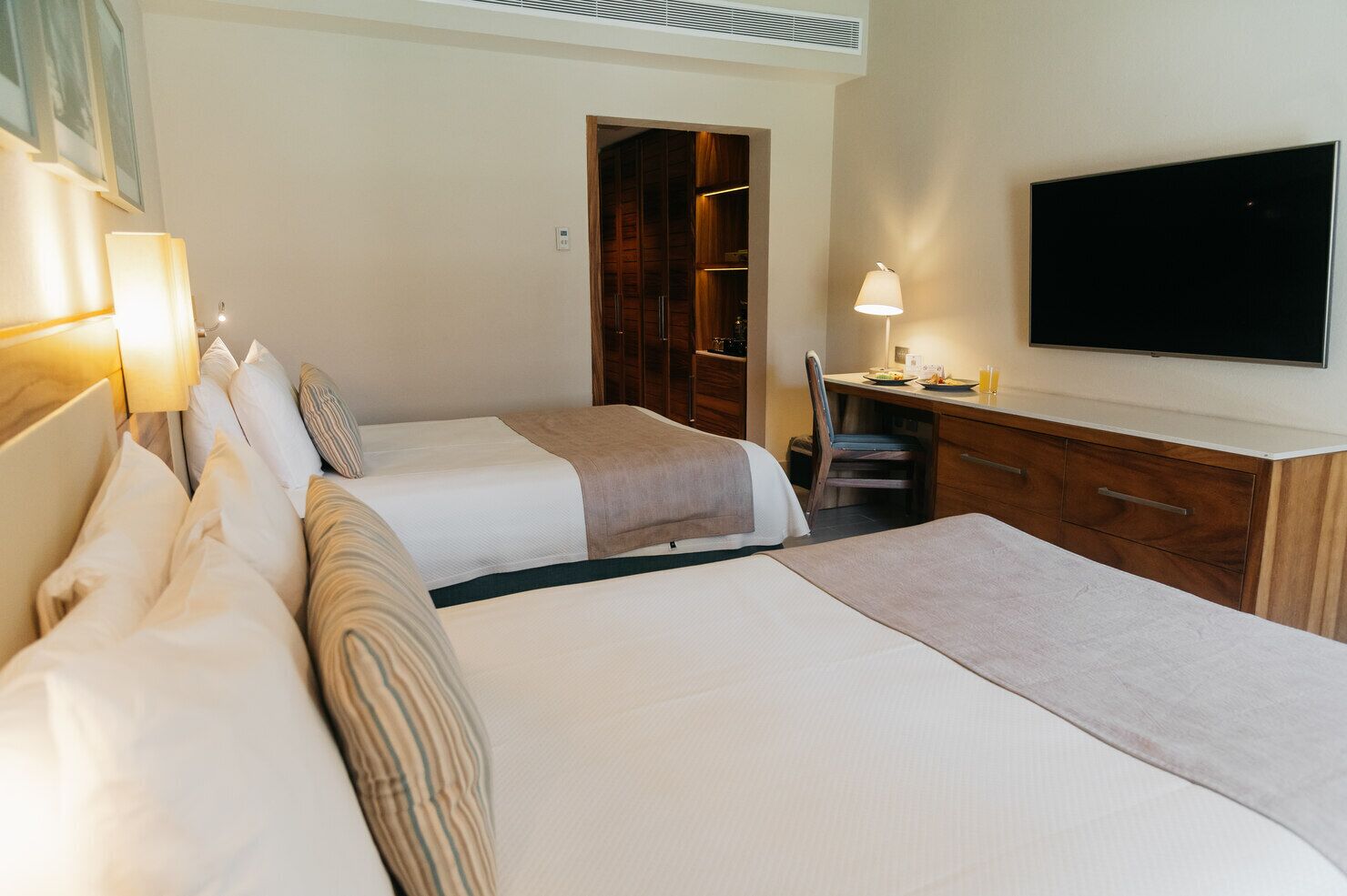 Ein Hotelzimmer mit zwei Betten, einem Schreibtisch, einem Stuhl, einem Fernseher und einem Kleiderschrank.