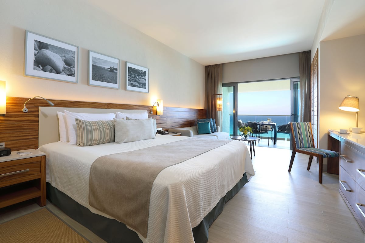 Habitación de hotel con una cama grande, un escritorio, una silla y un balcón con vistas al mar.