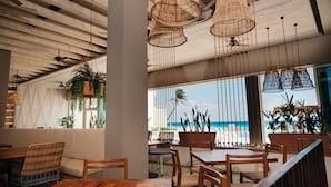 A restaurant with wooden furniture, hanging wicker chandeliers, and large windows overlooking the beach. - Emporio Cancun Optional All Inclusive (Cancun)