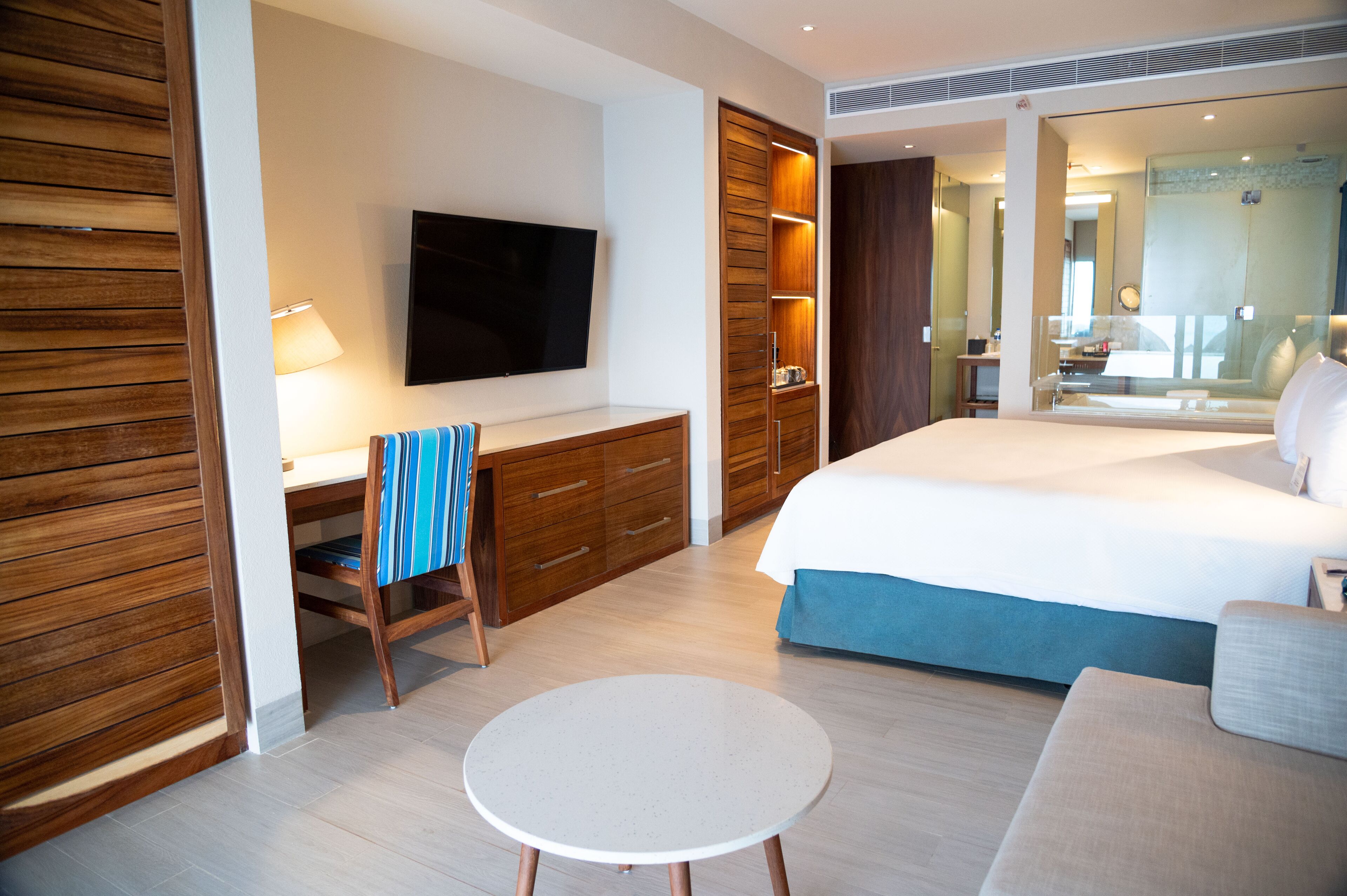 Une chambre d’hôtel comprenant un lit, un bureau avec une chaise, une télévision et une salle de bain visible à travers une porte en verre.