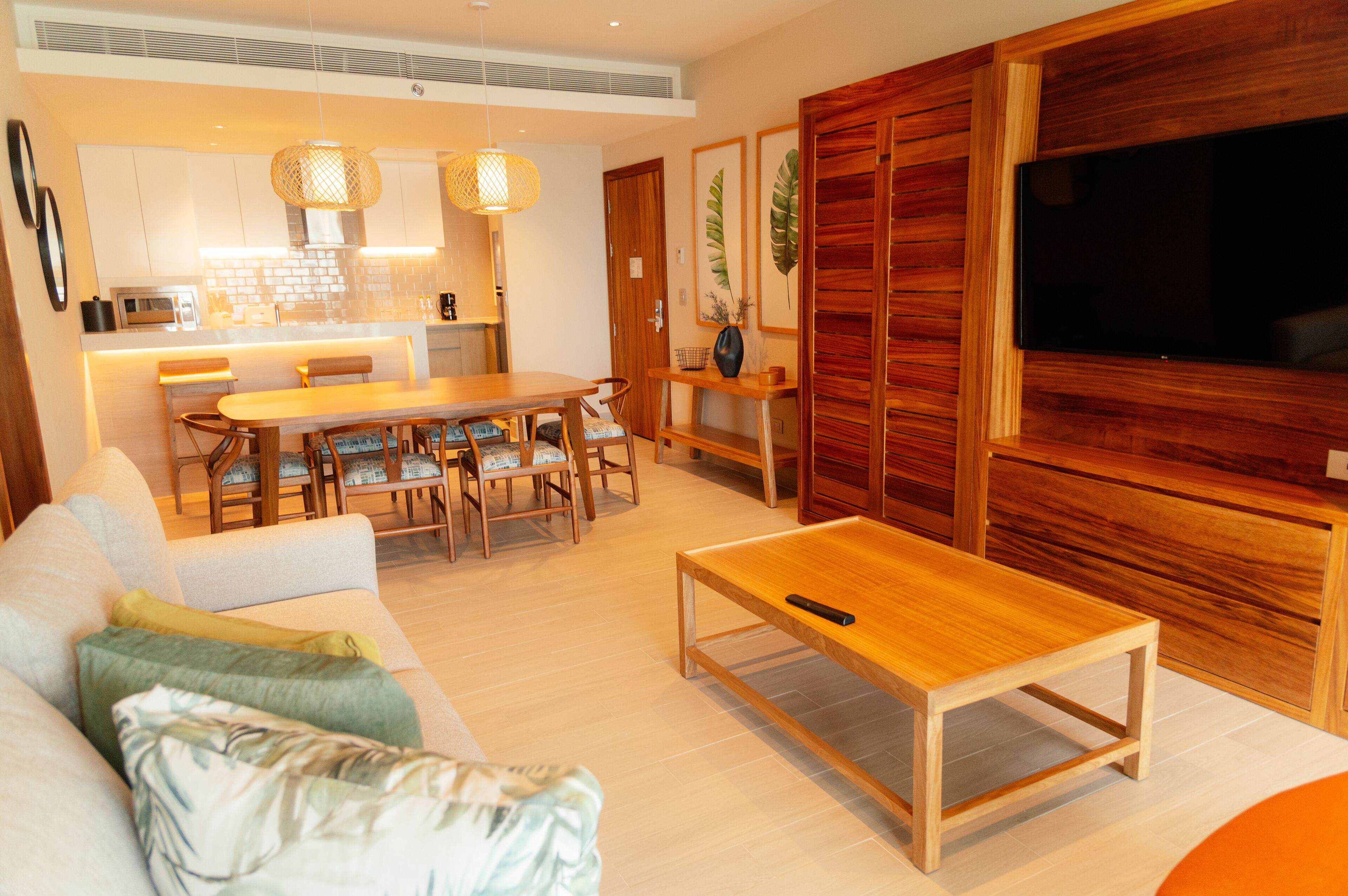 Una sala de estar moderna con una mesa de centro de madera, un sofá con cojines, una zona de comedor con una mesa y sillas de madera, y un televisor montado en una pared de madera.