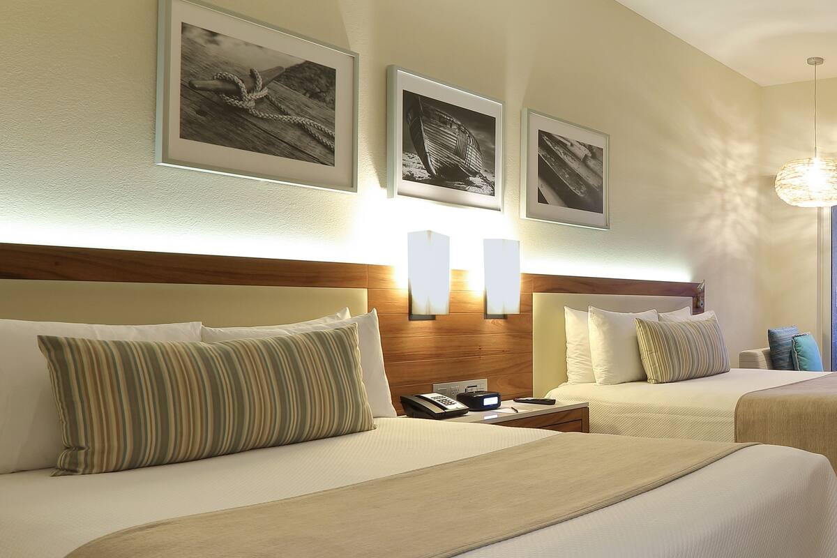 Habitación de hotel con dos camas, un cabecero de madera, una mesita de noche con un teléfono e iluminación montada en la pared.