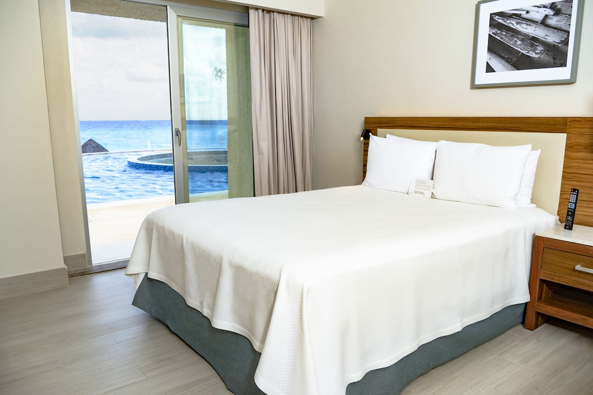 Habitación de hotel con cama, mesita de noche, control remoto y vista al océano a través de una puerta corredera.