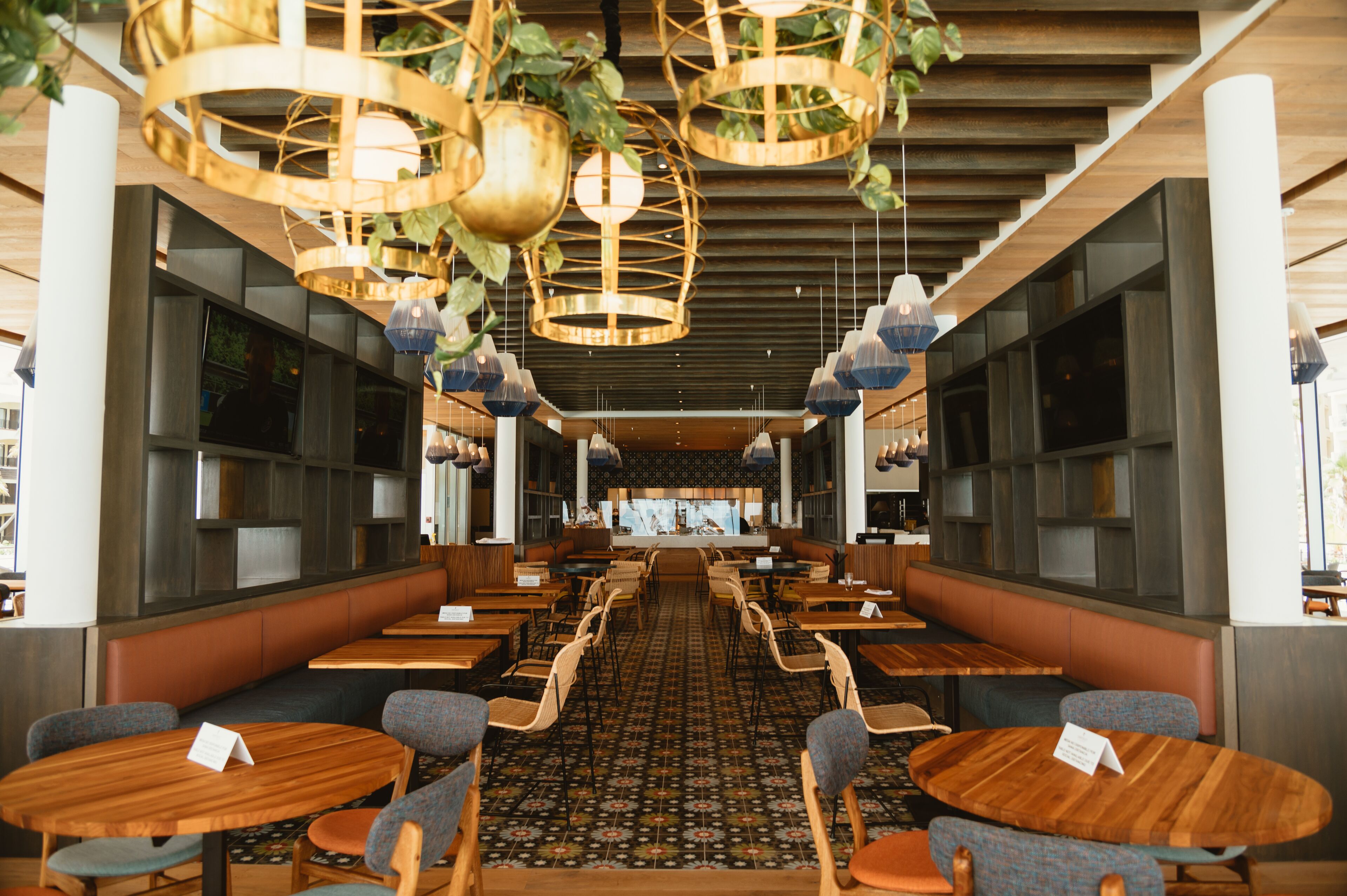 A spacious restaurant with high ceilings, wooden tables, and booths, featuring hanging pendant lights and a patterned floor.