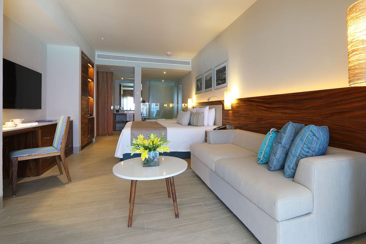 Habitación de hotel con cama, sofá, televisión, escritorio y baño a la vista.